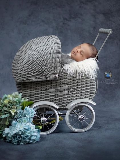 This newborn boy is sleeping in a grey pram against a deep blue backdrop, creating a classic and timeless portrait complemented by a bouquet of blue hydrangeas.