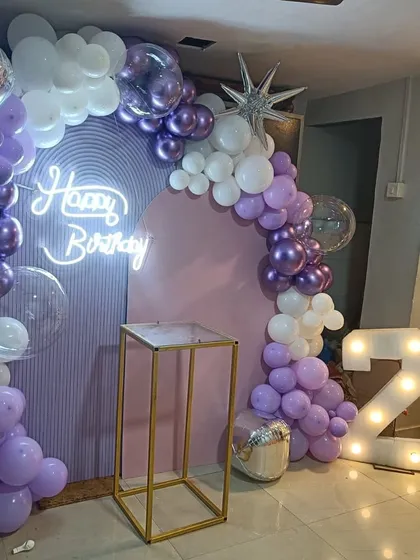 This 24th birthday setup features a modern arched backdrop in pastel purple. We decorated it with an organic balloon garland, a 'Happy Birthday' neon sign, and large '24' marquee numbers for a trendy and personalized celebration.