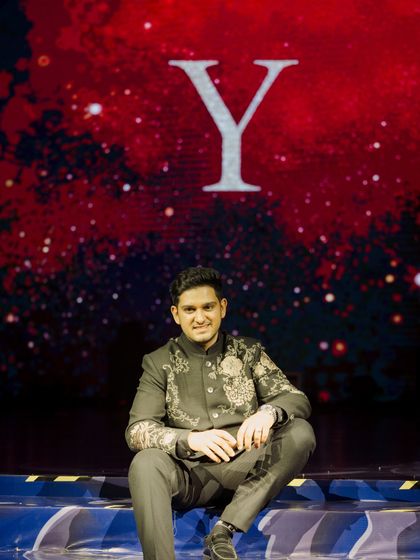 A quiet moment before the show. The groom sits on the edge of the stage, with his initial projected on the giant LED screen behind him, ready for his big performance.