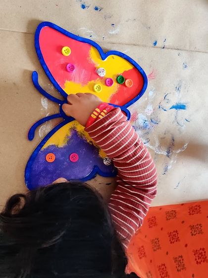 Another little artist having fun decorating a butterfly with paint and colorful buttons. It's a great sensory activity for toddlers.