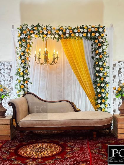 A classic and regal setup for a ring ceremony. The decor features a beautiful floral arch of white and yellow roses, a vintage-style chaise lounge, and a chandelier for a touch of royalty.