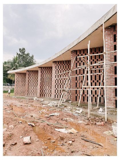 The curved brick facade of the auditorium under construction, with bamboo scaffolding still in place.