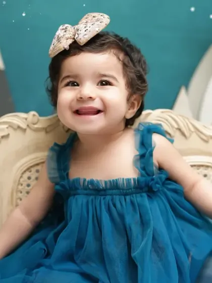 A close-up of a smiling toddler in a beautiful blue dress during her winter-themed milestone shoot. Her bright smile lights up the whole scene.