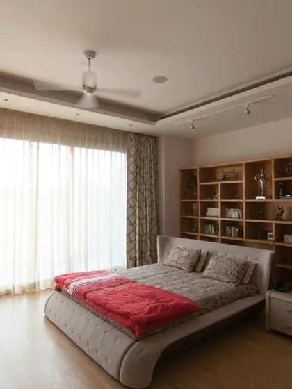 This bedroom is designed as a serene retreat. A large window offers an uninterrupted view of the greenery, while the built-in wooden shelving adds warmth and a place for personal belongings, making the space feel intimate and calm.