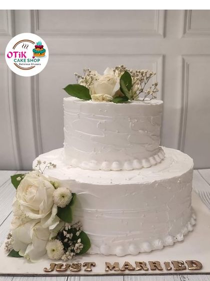 A classic two-tiered "Just Married" cake, perfect for an intimate wedding celebration. The textured white buttercream is adorned with fresh white roses for a look of pure and simple elegance.