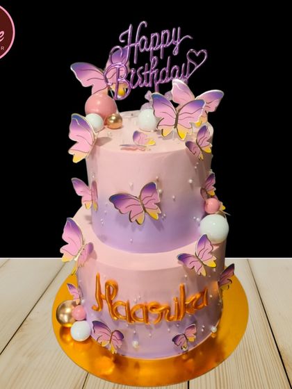 A beautiful two-tiered butterfly theme cake in shades of pink and purple. The delicate, fluttering butterflies create a sense of movement and whimsy, perfect for a dreamy birthday celebration.