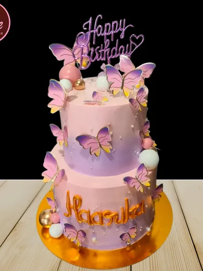 This two-tiered butterfly cake features a beautiful purple and pink ombre effect. The delicate, fluttering butterflies create a sense of movement and wonder.