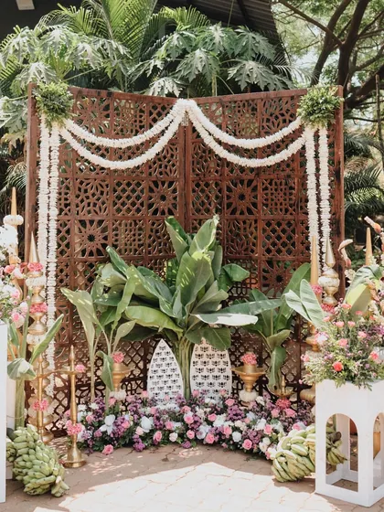 A detailed view of a traditional decor setup, featuring a carved wooden backdrop, garlands of fresh jasmine, and lush banana plants. These elements come together to create an authentic and sacred ambiance.