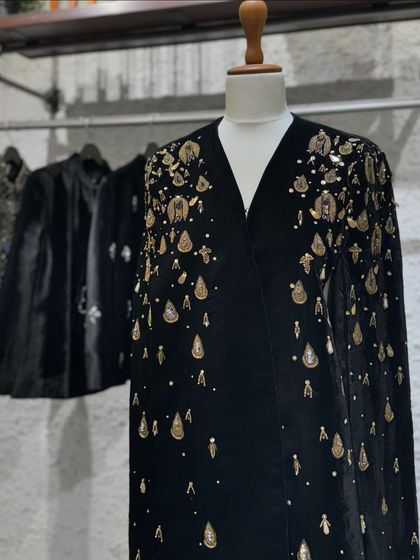 A luxurious black velvet cape with intricate gold teardrop embellishments, a perfect layering piece for winter festivities.