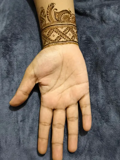 The back of the hand, showing a simple cuff with peacock and checkerboard patterns.