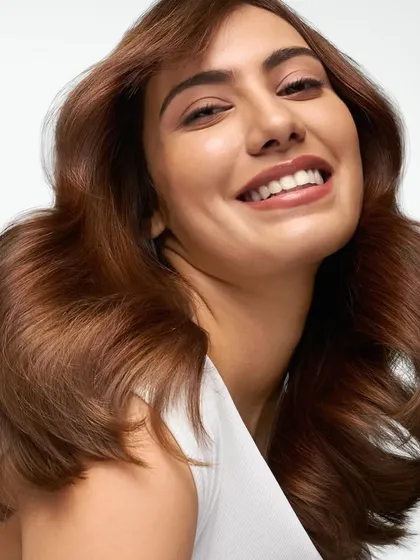A clean, luminous studio photograph for a Dove haircare campaign. This image captures a model with healthy, voluminous brown hair and a joyful expression, highlighting the product's ability to create shine and vitality. The bright, high-key lighting is characteristic of my advertising work for major FMCG brands.