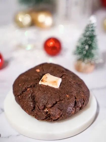 A single, chunky s'mores cookie with a toasted marshmallow on top. The simple, clean styling on a marble coaster highlights the cookie's delicious simplicity.