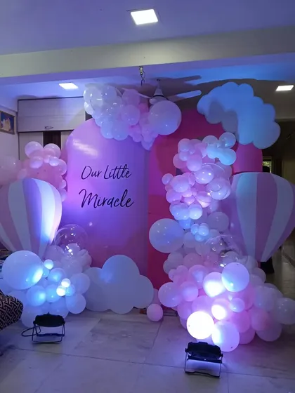 A pink hot air balloon theme for a baby girl's celebration. The "Our Little Miracle" backdrop is surrounded by pink and white balloons shaped like clouds, creating a sweet, sky-like scene.