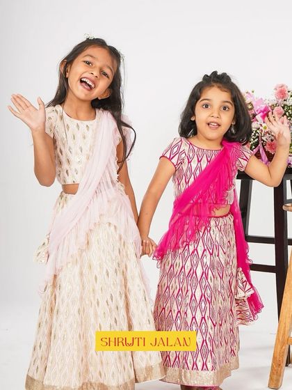 These sisters are all smiles in their coordinated printed lehengas. The modern silhouette with a pre-draped ruffled dupatta makes it a stylish and hassle-free option for young girls.
