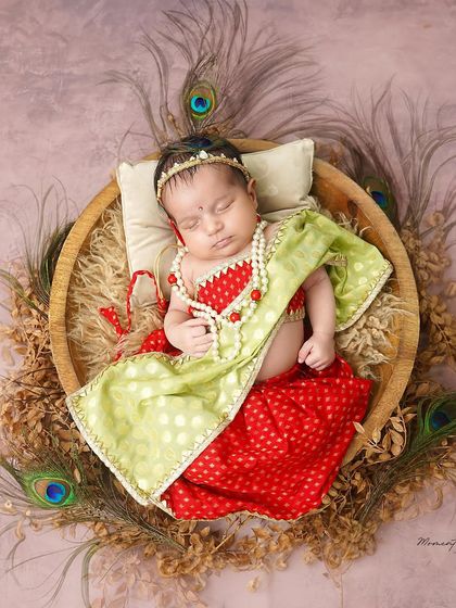 A divine little Radha. This newborn girl is dressed in a beautiful traditional outfit, complete with tiny jewelry and peacock feathers, for a culturally rich portrait.