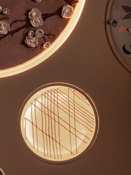 A detail of the custom fabric mural in Zone One. This composition of three circular panels includes an embossed bird, floral embroidery, and sheer fabric, all backlit to create a soft glow. It’s a piece of art that tells the brand's story through texture.