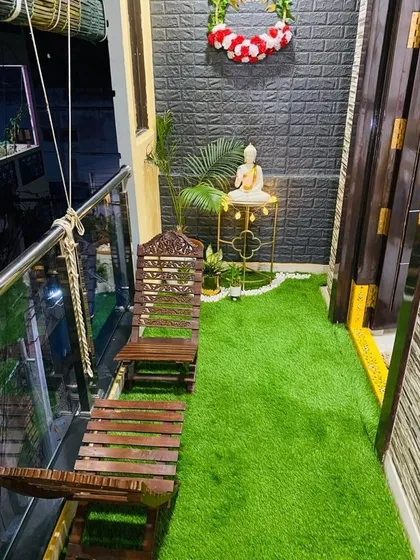 Even a small balcony can become a peaceful retreat. Here, we used artificial grass, a small Buddha statue on an elegant stand, and simple wooden chairs to create a cozy and calm corner.