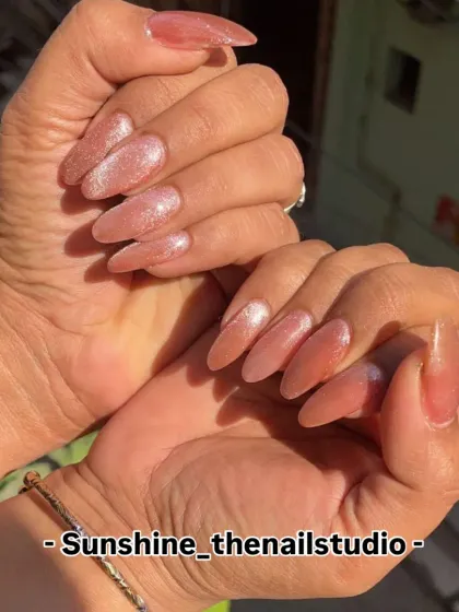 A beautiful set of long, almond-shaped nails with a shimmery pink glitter polish.