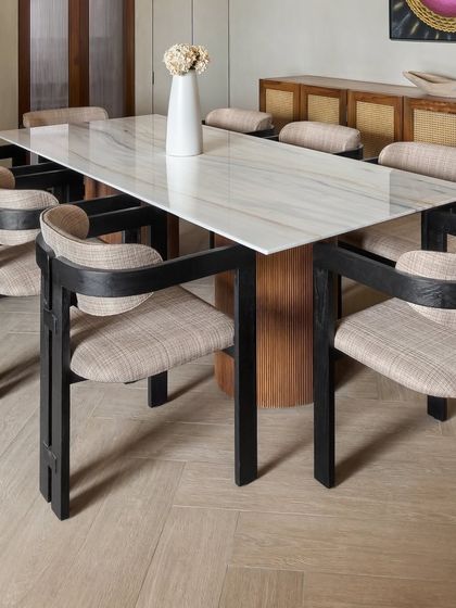 The dining chairs at the East Coast Residence feature a unique design with black-lacquered frames and woven seats, adding a layer of texture and graphic contrast to the room.