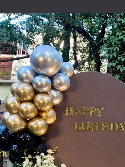 A simple and elegant "Happy Birthday" sign on a modern backdrop, part of the 75th birthday celebration decor. The gold and silver balloon accent adds a festive touch.