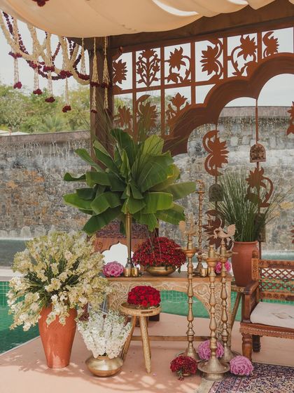 A decor corner by the pool, featuring banana plants, brass candelabras, and red flowers.