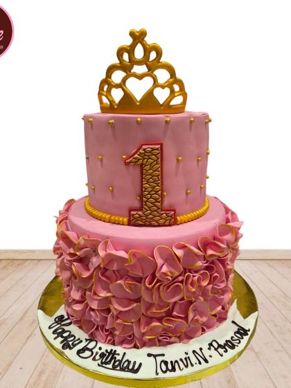 Perfect for a first birthday, this two-tiered pink princess cake is decorated with a golden crown and elegant ruffles. The textured number '1' adds a special touch for the big milestone.