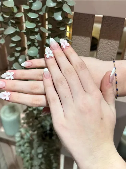 A beautiful example of bridal nails, featuring a soft ombré base with delicate 3D flowers and bows.