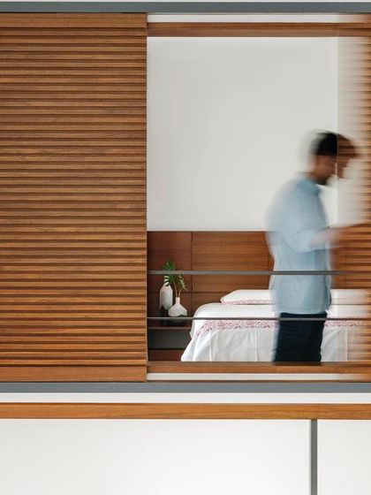 A detail of the sliding wooden louvers in the 'Copper House'. This element allows for a playful interaction with light and privacy, casting patterns across the interior while offering glimpses into the space beyond.