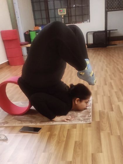 This is an advanced backbend, bringing the feet towards the head from a forearm wheel pose, supported by a yoga wheel. This shows the incredible spinal flexibility that can be achieved with dedicated practice.