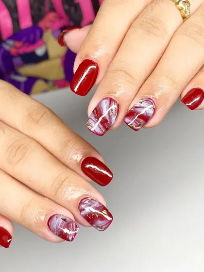 A beautiful red and white marble design with gold foil accents on short, square nails.