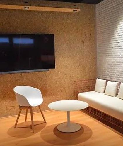 The reception area features a custom-designed wireframe sofa and a wall of raw pressed board. A large piece of monochrome art adds a powerful graphic element against the textured white brick wall.