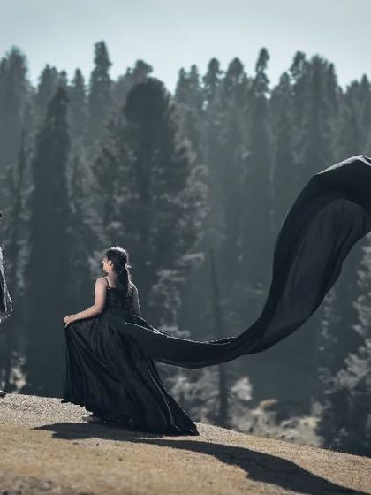 A dramatic, high-fashion shot in the mountains. The long, flowing black gown against the backdrop of the pine forest creates a stunning and powerful image.
