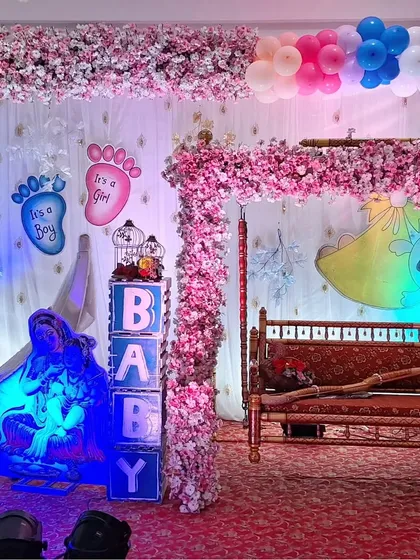A traditional baby shower setup featuring a beautifully decorated wooden cradle (jhula). The decor includes 'BABY' light blocks, a cutout of Lord Krishna, and floral arrangements, blending modern and classic elements.