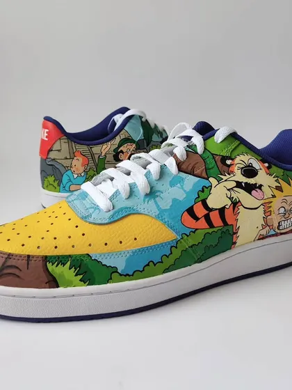 A nostalgic mashup of The Adventures of Tintin and Calvin and Hobbes on a pair of Nike Court Vision Lows. This shoe features Calvin and his tiger Hobbes in their classic chaotic style.