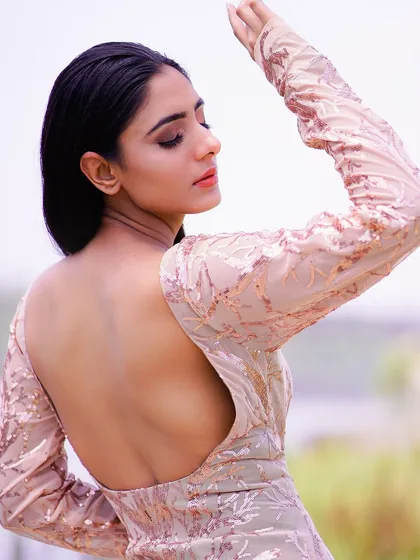 A stunning profile shot of a model in a backless, sequined gown, with the sun highlighting her features. The natural backdrop of water and trees adds a touch of serenity to this glamorous photo.