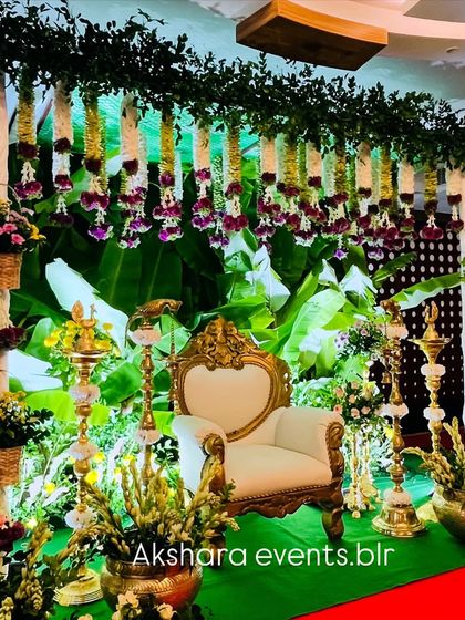 A beautiful Seemantham setup featuring a lush banana leaf backdrop, hanging floral garlands, and an ornate chair. The warm lighting creates a festive and inviting atmosphere.