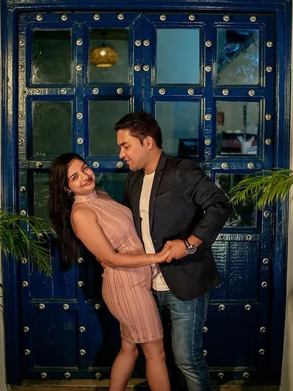 A fun, dance-like pose against a vibrant blue door. The architectural details and lighting add a quirky, charming character to this evening pre-wedding photo.