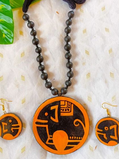 Inspired by temple carvings, this hand-painted elephant pendant has a bold, graphic style. The orange and black combination is striking, and the earrings feature a stylized elephant head.