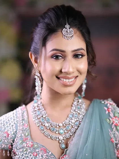 A smiling model wearing a beautiful layered zircon necklace with light blue stones, perfectly matching her lehenga.