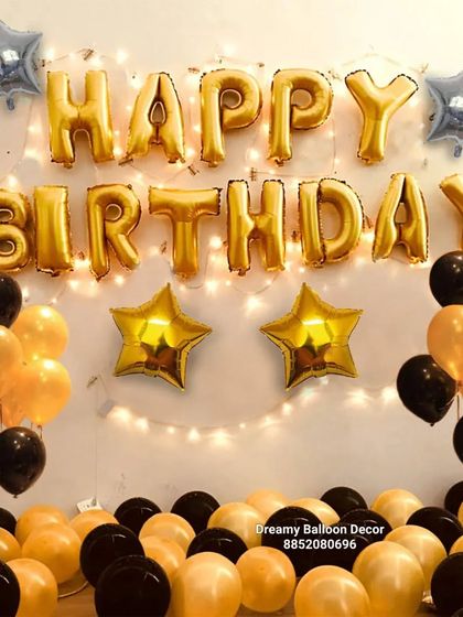 A classic black and gold 'Happy Birthday' wall decoration. This simple setup with foil balloons and fairy lights is an easy way to add a festive touch to any room.