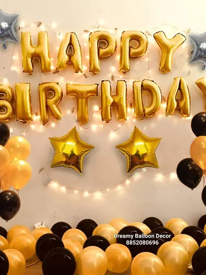 A classic black and gold 'Happy Birthday' wall decoration. This simple setup with foil balloons and fairy lights is an easy way to add a festive touch to any room.