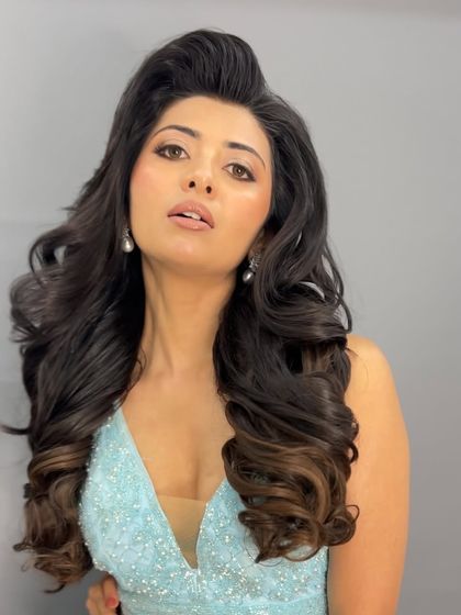 A glamorous, high-volume hairstyle with a side part and big, bouncy curls, perfect for a red-carpet or reception look.