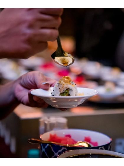 A chef adds a final drizzle of sauce to a sushi roll before serving it to a guest, highlighting the finishing touches.