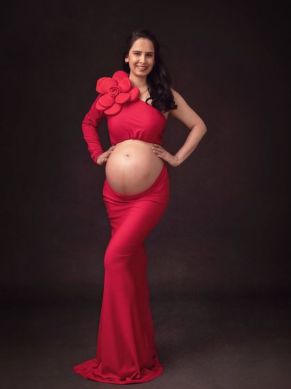 A bold and stylish portrait. The red cutout gown is accented with a large floral piece on the shoulder, adding a high-fashion touch to the maternity shoot.