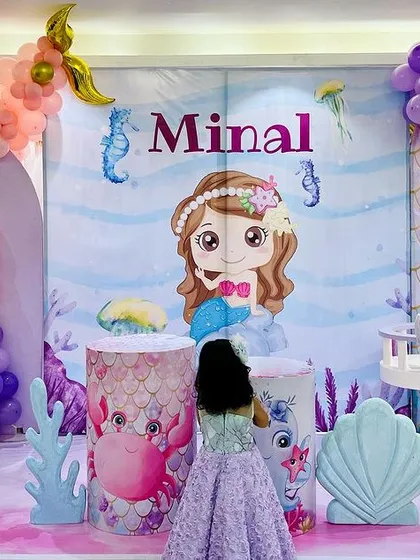 Little mermaid Minal enjoying her special day. This photo captures the birthday girl in front of her elaborate mermaid-themed stage, complete with character backdrops and a light-up number '3'.
