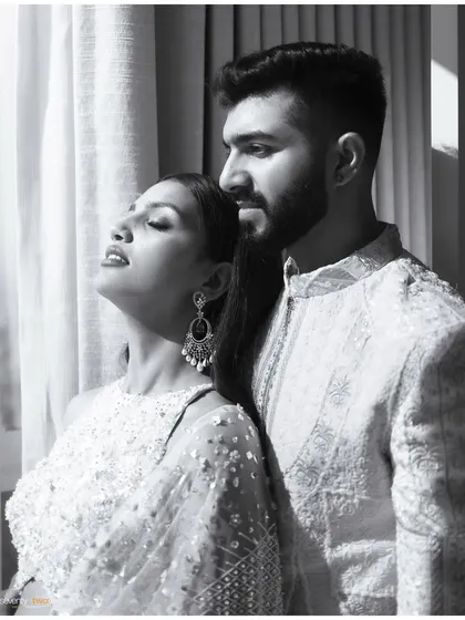 A serene black and white portrait of a couple, bathed in soft window light. Her eyes are closed in contentment as she leans into him.
