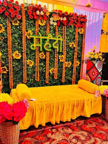 For this Mehendi ceremony, I used a lush artificial green wall as the base. I decorated it with vertical marigold garlands and a custom 'Mehendi' sign made of flowers, creating a fresh, nature-inspired look. The yellow seating provides a beautiful contrast for the bride.