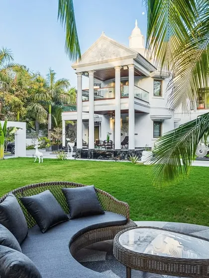 A daytime view of the circular deck at 'Tropical Manor'. The space is designed for tranquility, surrounded by a lush lawn and framed by the modern gothic architecture of the villa, creating an immersive connection with nature.