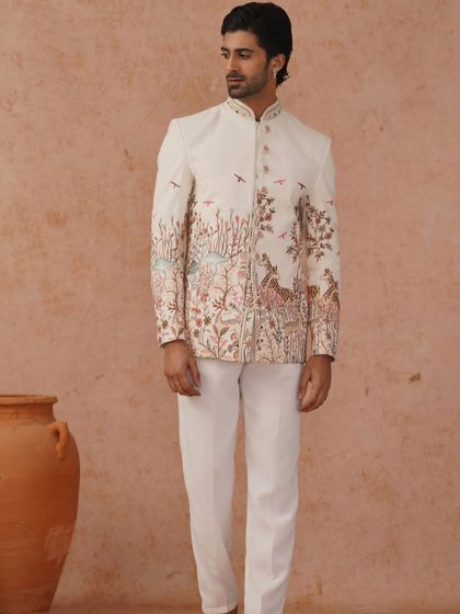 A professional shot of a model in a unique embroidered Jodhpuri suit. The nature-inspired embroidery along the bottom adds an artistic and whimsical touch.