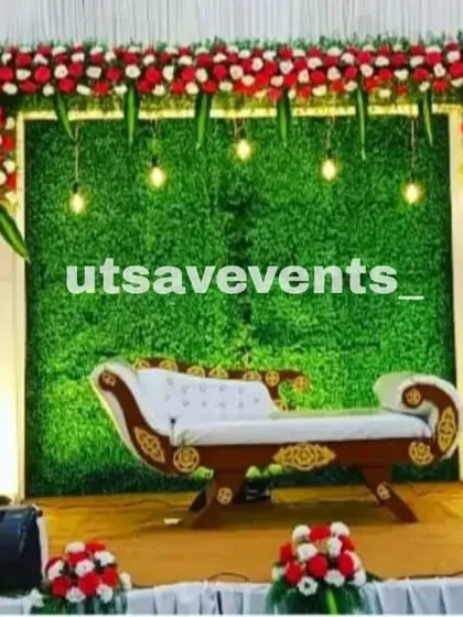 A simple and classic reception stage with a greenery wall and a red and white floral border. The hanging lights add a warm and inviting glow.